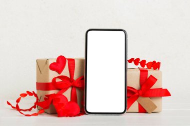 mobile phone with blank screen on colored background with hearts, calendar and gift box, valentine day concept perspertive view flat lay.