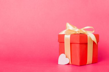 gift box with red bow and red heart on colored background. Perspective view. Flat lay.