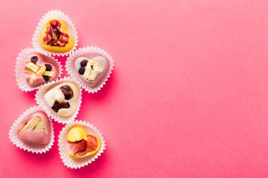 chocolate sweets in the form of a heart with fruits and nuts on a colored background. top view with space for text, holiday concept.