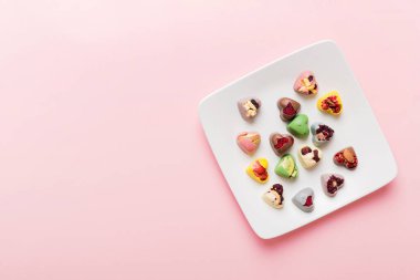 Plate with different chocolate on colored background. Assortment of fine chocolates top view vith copy space Health and obesity concept.