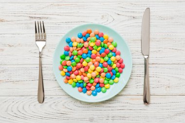 cutlery on table and sweet plate of candy. Health and obesity concept, top view on colored background.