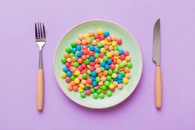 cutlery on table and sweet plate of candy. Health and obesity concept, top view on colored background.
