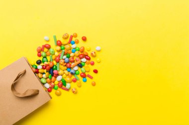 shopping paper gift bag in corner full of assorted traditional candies falling out on colored background with copy space. Happy Holidays sale concept.