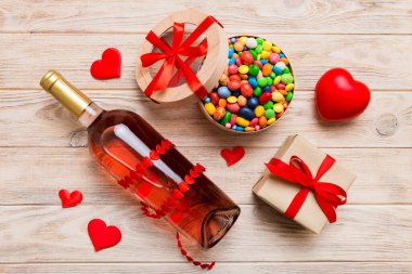 Sevgililer Günü için renkli arka planda bir şişe kırmızı şarap hediye ve çikolatalı. Kalp, hediye kutusuyla şekillendirilmiş çikolatalar fotokopi alanı ile üst görünüm.