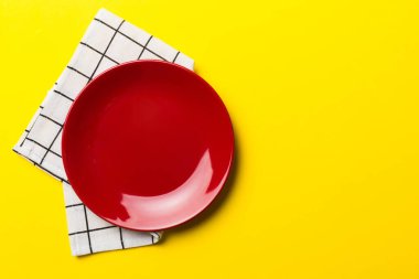 Renkli arka planda üst görünüm yiyecek için masa örtüsü üzerindeki boş yuvarlak kırmızı tabak. Tasarımınız için boşluk olan peçeteye boş tabak.
