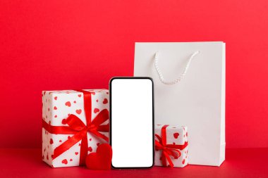 mobile phone with blank screen on colored background with hearts, calendar and gift box, valentine day concept perspertive view flat lay.