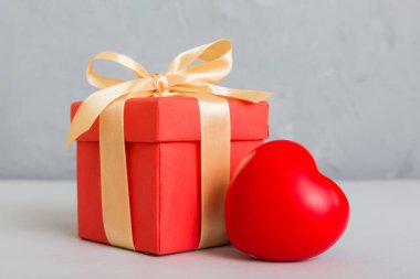 gift box with red bow and red heart on colored background. Perspective view. Flat lay.