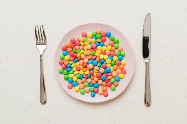 cutlery on table and sweet plate of candy. Health and obesity concept, top view on colored background.