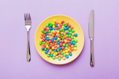 cutlery on table and sweet plate of candy. Health and obesity concept, top view on colored background.