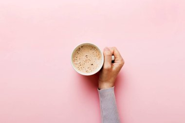 Renkli arka planda bir fincan kahve tutan minimalist stil bir kadın. Düz yerde, kapuçino bardağının üstünde. Metin için boş yer, kopyalama alanı. Kahve bağımlılığı. Üst manzara, düz uzanma.