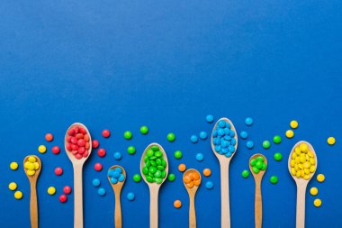 Renkli arka planda kaşık üzerinde renkli tatlı şekerler. Fotokopi alanı ile şekerleme dekoru üst görünümü.