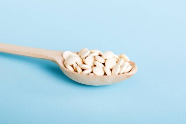 Heap of white pills on colored background. Tablets scattered on a table. Pile of red soft gelatin capsule. Vitamins and dietary supplements concept.