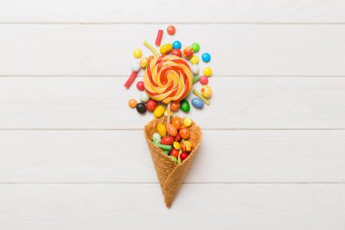 waffle cone full of assorted traditional candies falling out on colored background with copy space. Happy Holidays sale concept.