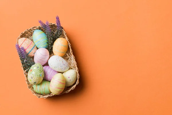 stock image Colorful Easter eggs in wicker basket against colored background, closeup. top view with copy space.