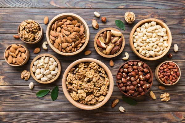 mixed nuts in wooden bowl. Mix of various nuts on colored background. pistachios, cashews, walnuts, hazelnuts, peanuts and brazil nuts.