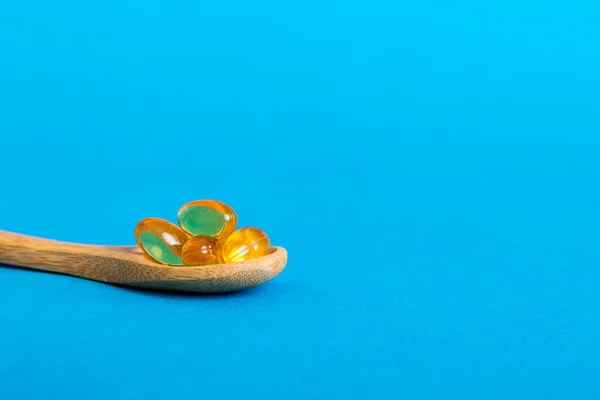 Vitamin omega capsules in a spoon on a colored background. Pills served as a healthy meal. Red soft gel vitamin supplement capsules on spoon.
