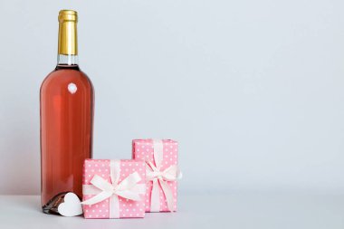 Bottle of wine on colored background for Valentine Day with gift box. Heart shaped with presrnt box perspective view with copy space.