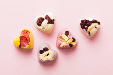 chocolate sweets in the form of a heart with fruits and nuts on a colored background. top view with space for text, holiday concept.