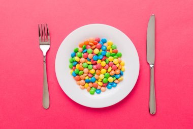 cutlery on table and sweet plate of candy. Health and obesity concept, top view on colored background.