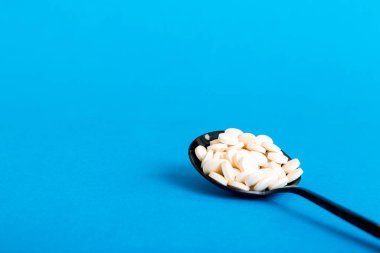 Heap of white pills on colored background. Tablets scattered on a table. Pile of red soft gelatin capsule. Vitamins and dietary supplements concept.