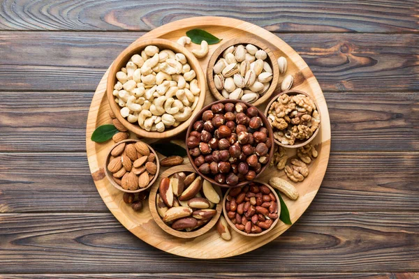 mixed nuts in wooden bowl. Mix of various nuts on colored background. pistachios, cashews, walnuts, hazelnuts, peanuts and brazil nuts.
