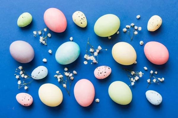 Happy Easter composition. Easter eggs on colored table with gypsophila. Natural dyed colorful eggs background top view with copy space.