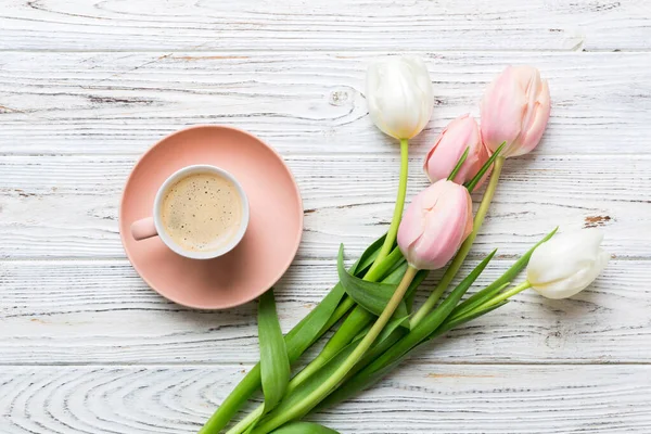Spring background with flowers, a cup of coffee and a bouquet of pink and white tulips on colored table background with place for text. Copy space top view.