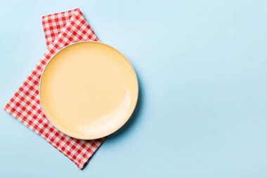 Renkli arka planda üst manzara. Yemek için masa örtüsü üzerinde boş yuvarlak sarı tabak. Tasarımınız için boşluk olan peçeteye boş tabak.