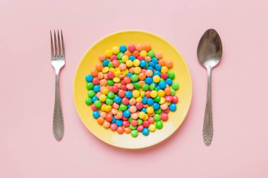 cutlery on table and sweet plate of candy. Health and obesity concept, top view on colored background.