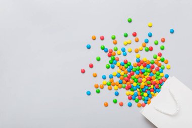 shopping paper gift bag in corner full of assorted traditional candies falling out on colored background with copy space. Happy Holidays sale concept.