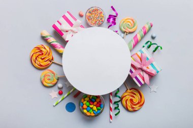 Tatil kompozisyonu yatıyordu. Kağıt boş, lolipop, renkli arka planda doğum günü süslemeleri. Üst görünüm, metin için boşluk kopyala.