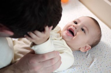 Mutlu baba ve oğul evde eğleniyor. Baba ve bebek yatak odasında, parlak bir arka planda. Şefkat, ebeveynlik.