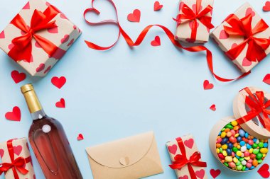 top view photo of st valentine day decor shopping, bag, wine, bottle, envelope, gift, box, candy and red heart on colored background with empty space. Frame background.