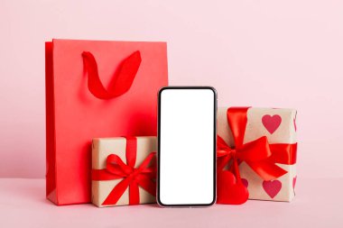 mobile phone with blank screen on colored background with hearts, calendar and gift box, valentine day concept perspertive view flat lay.