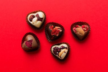 chocolate sweets in the form of a heart with fruits and nuts on a colored background. top view with space for text, holiday concept.