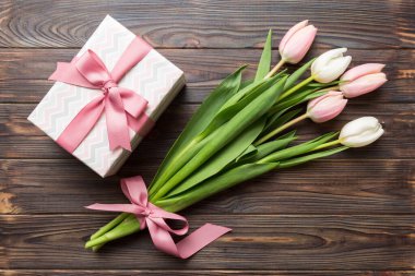 Pembe lale çiçekleri ve hediye ya da renkli masa arkaplanındaki hediye kutusu. Anneler günü, doğum günü, kadınlar günü, kutlama konsepti. Metin üstü görünümü için boşluk.