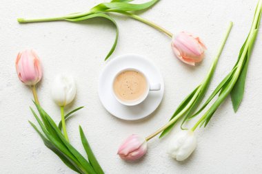 Çiçeklerle dolu bahar arkaplanı, bir fincan kahve ve renkli masa arkaplanlı pembe ve beyaz laleler. Üst görünümü kopyala.