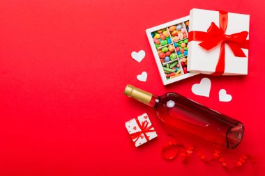 Sevgililer Günü için renkli arka planda bir şişe kırmızı şarap hediye ve çikolatalı. Kalp, hediye kutusuyla şekillendirilmiş çikolatalar fotokopi alanı ile üst görünüm.