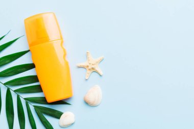 Sunscreen spray bottle. Bottle with sun protection cream and sea shells with tropical green leaf on color background, top view.