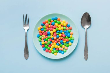 cutlery on table and sweet plate of candy. Health and obesity concept, top view on colored background.