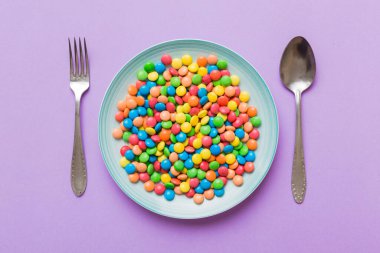cutlery on table and sweet plate of candy. Health and obesity concept, top view on colored background.