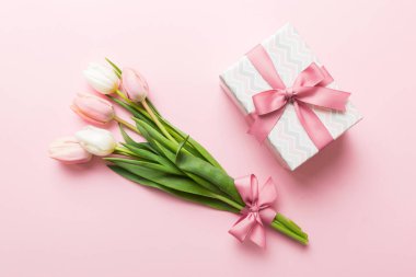 Pembe lale çiçekleri ve hediye ya da renkli masa arkaplanındaki hediye kutusu. Anneler günü, doğum günü, kadınlar günü, kutlama konsepti. Metin üstü görünümü için boşluk.