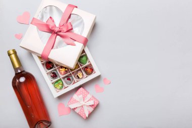 Sevgililer Günü için renkli arka planda bir şişe kırmızı şarap hediye ve çikolatalı. Kalp, hediye kutusuyla şekillendirilmiş çikolatalar fotokopi alanı ile üst görünüm.