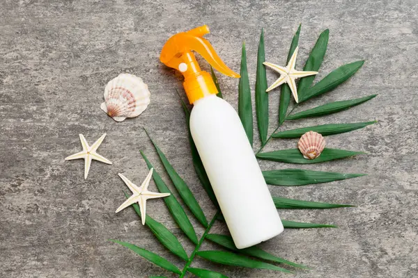 Sunscreen spray bottle. Bottle with sun protection cream and sea shells with tropical green leaf on color background, top view.