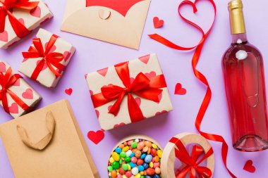 top view photo of st valentine day decor shopping, bag, wine, bottle, envelope, gift, box, candy and red heart on colored background with empty space. Frame background.