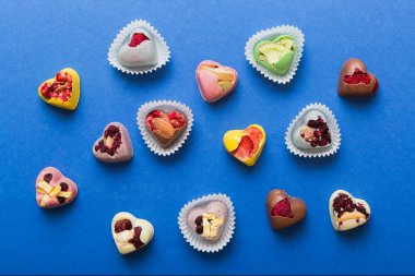 chocolate sweets in the form of a heart with fruits and nuts on a colored background. top view with space for text, holiday concept.