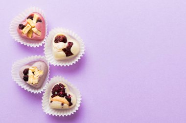 chocolate sweets in the form of a heart with fruits and nuts on a colored background. top view with space for text, holiday concept.