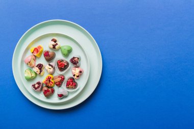 Plate with different chocolate on colored background. Assortment of fine chocolates top view vith copy space Health and obesity concept.