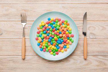 cutlery on table and sweet plate of candy. Health and obesity concept, top view on colored background.