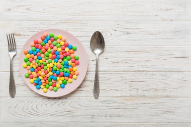 cutlery on table and sweet plate of candy. Health and obesity concept, top view on colored background.
